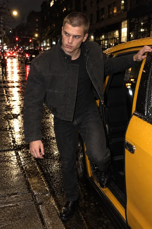 Concept render of NO SERVICE: a man with a buzz cut steps out of a taxi on a wet street at night, wearing a cropped charcoal utility jacket with a high collar and an offset zip.